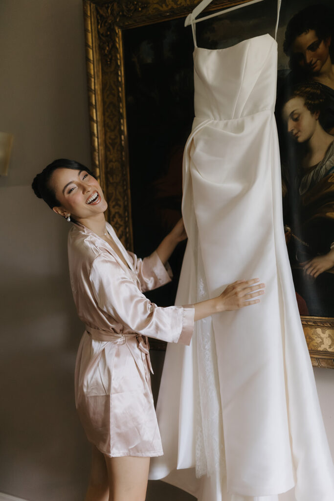 Bride in the getting ready moment with a hanging wedding dress in a stylish room