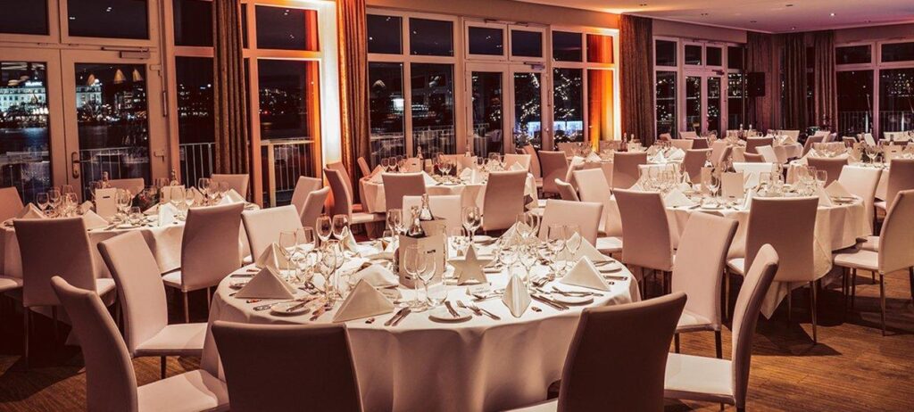 Hochzeitsdinner im Hamburger & Germania Ruder Club am Abend mit runden Tischen, warmer Lichtstimmung und Alsterblick