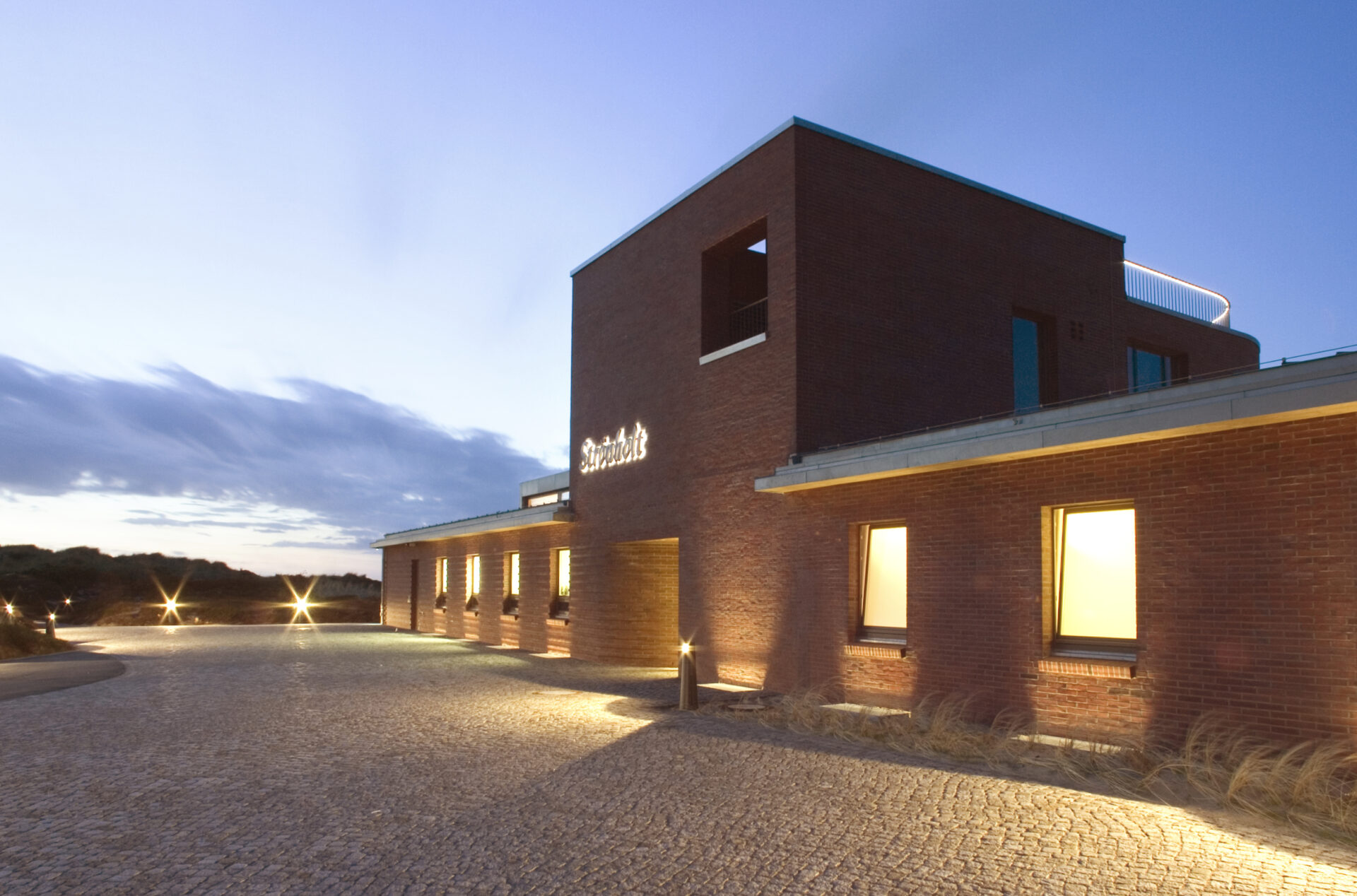 Außenansicht der Eventlocation Strönholt auf Sylt bei Abenddämmerung mit moderner Backsteinarchitektur und beleuchtetem Eingangsbereich