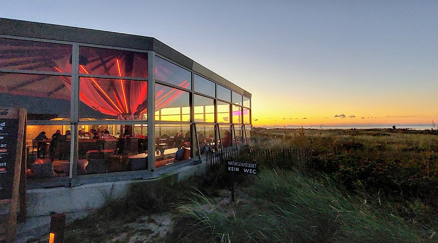 Sunset Lounge der Sturmhaube auf Sylt mit Glasfront und Blick auf die Dünenlandschaft bei Sonnenuntergang